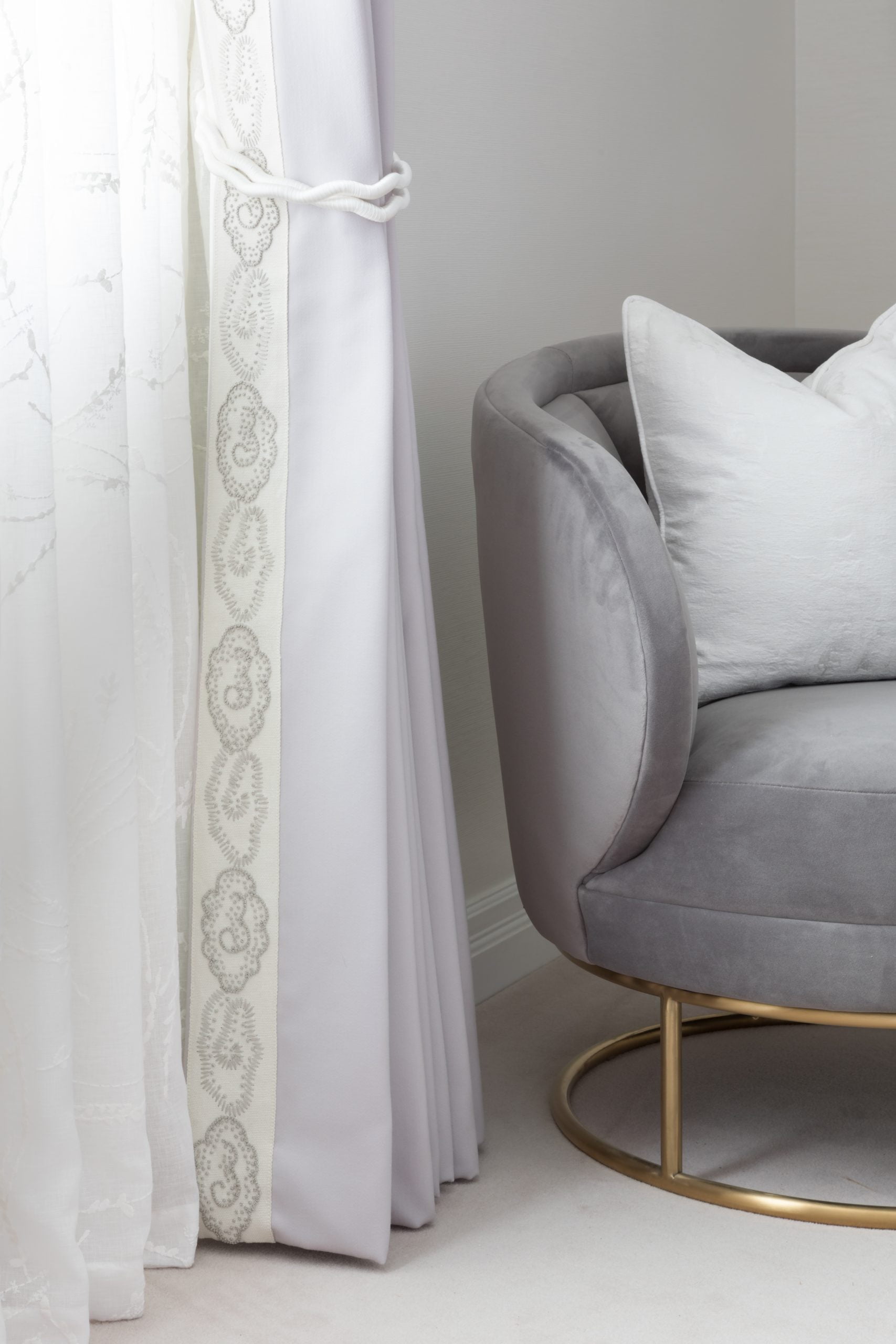Rounded suede armchair with white cushion and white patterned curtain tied up
