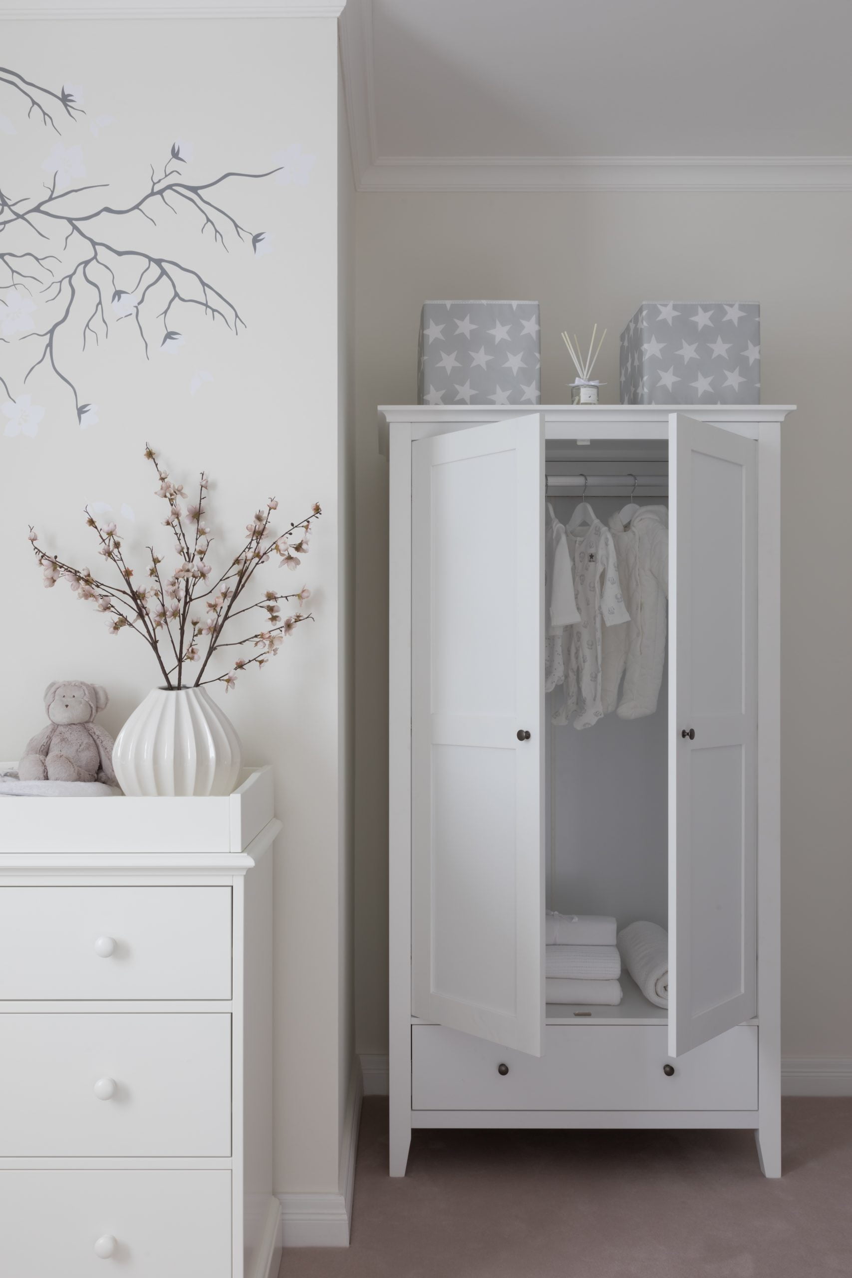 White wardrobe in Surrey filled with white baby clothing and two boxes on top with stars and diffuser between.