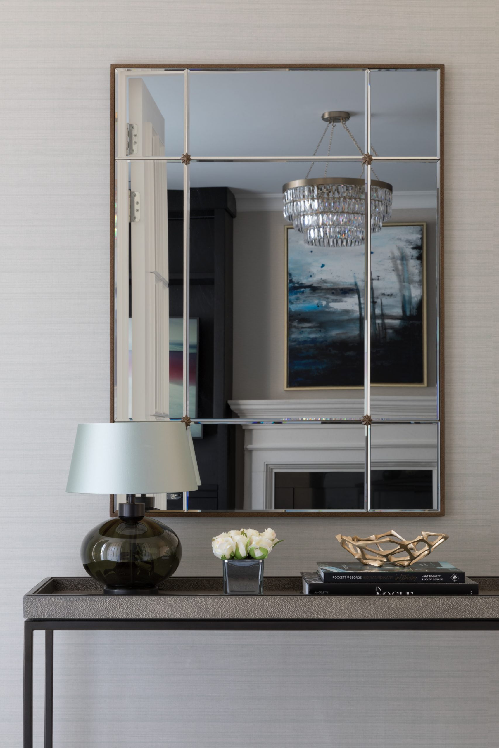 Freestanding console table with sectioned mirror above reflecting a glass chandelier and moody artwork