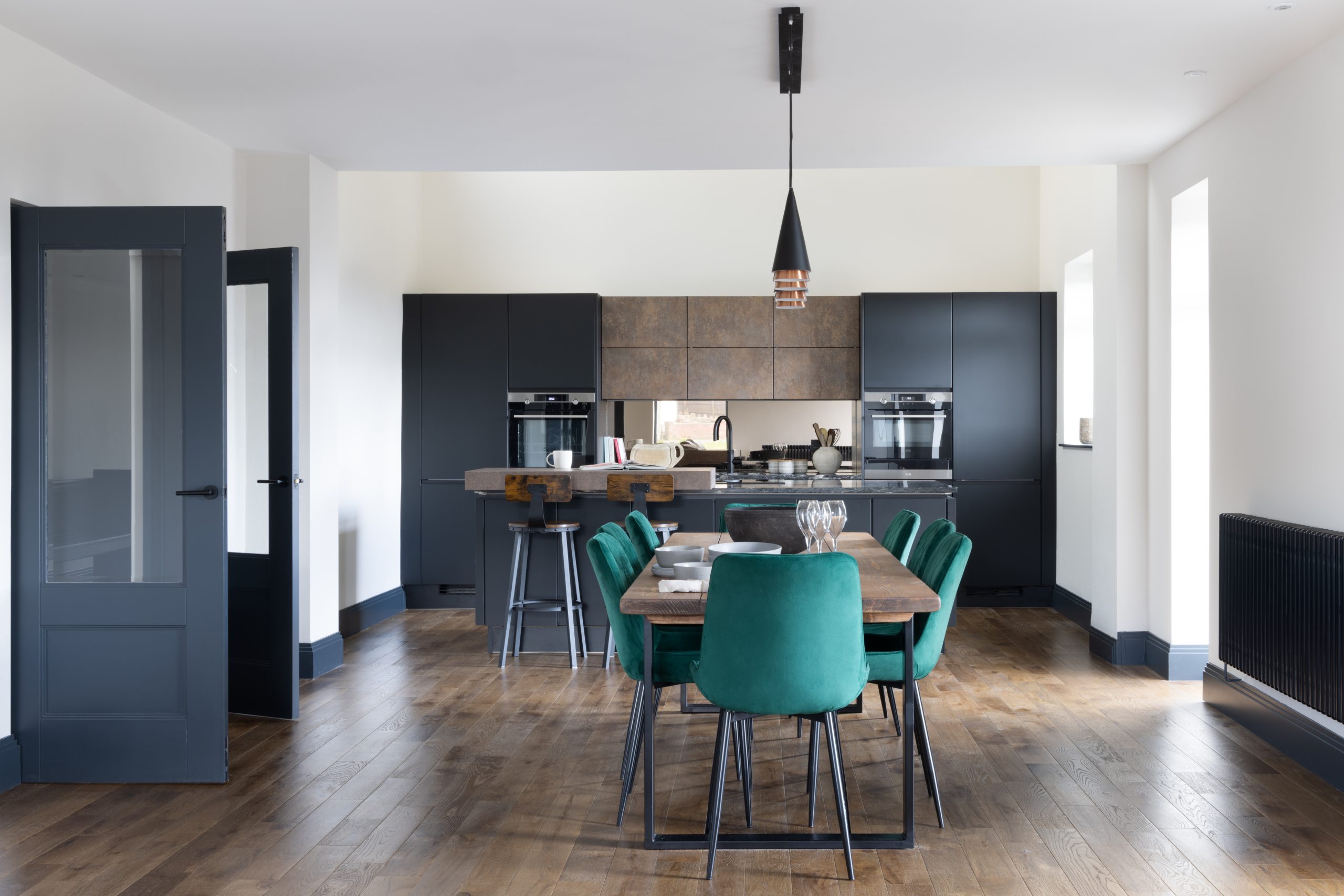 Long shot of contemporary kitchen with kitchen unit to back wall and long table with jade coloured chairs