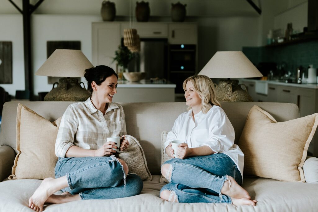 Emily and Danielle sitting on large sofa smiling at each other